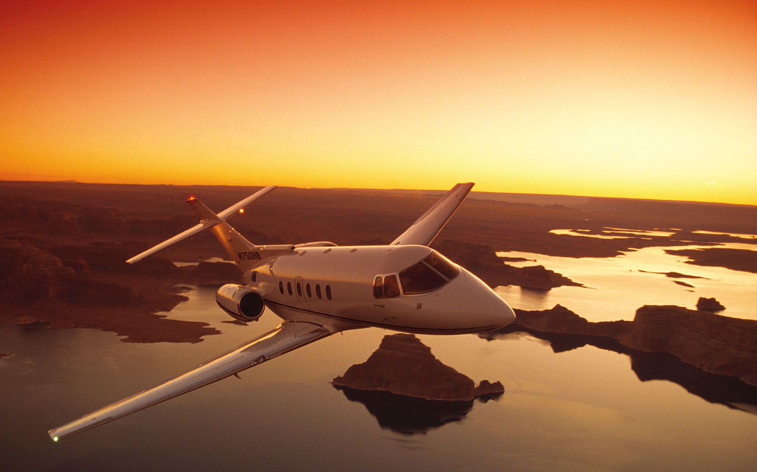 Hawker 750 private jet charter flying over canyon during golden sunset